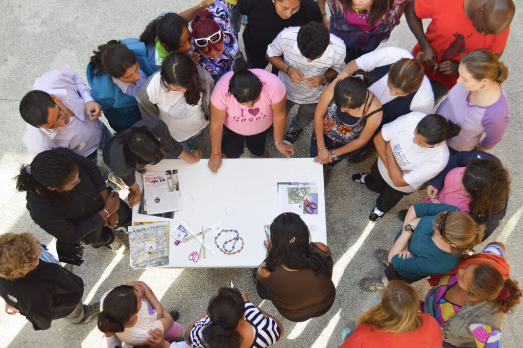 An aerial view of a workshop table where a group of artists teach how to make paper beads