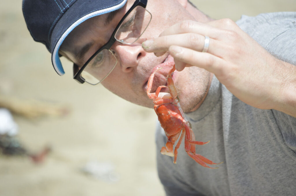 A man sticks out his tongue at a crab as he lifts it in the air