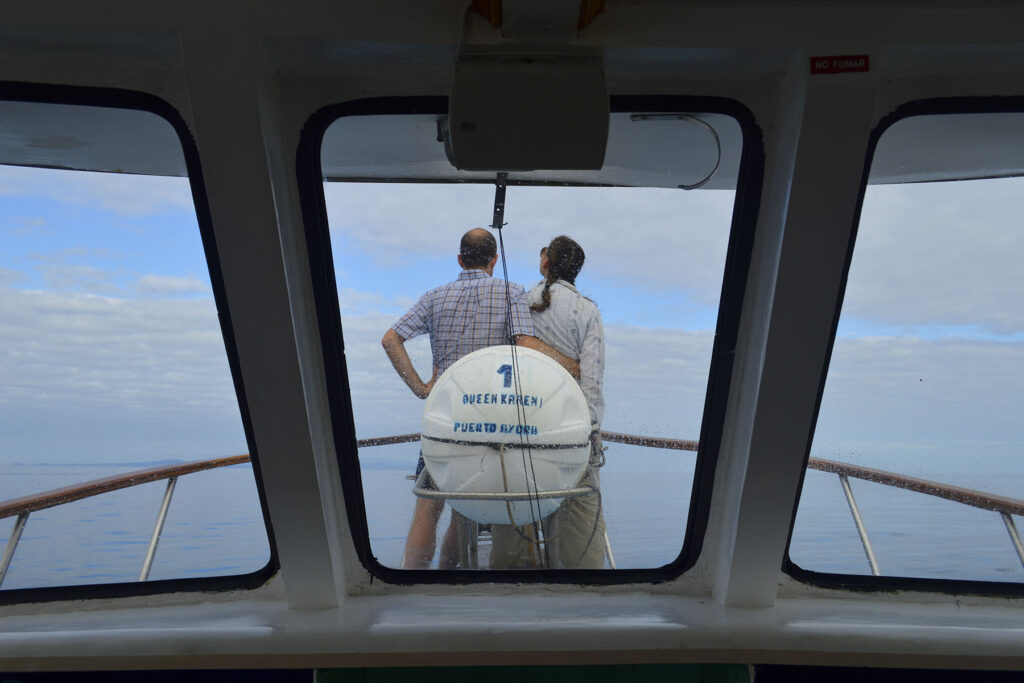 Two people seen through a window stand at the bow of a boat