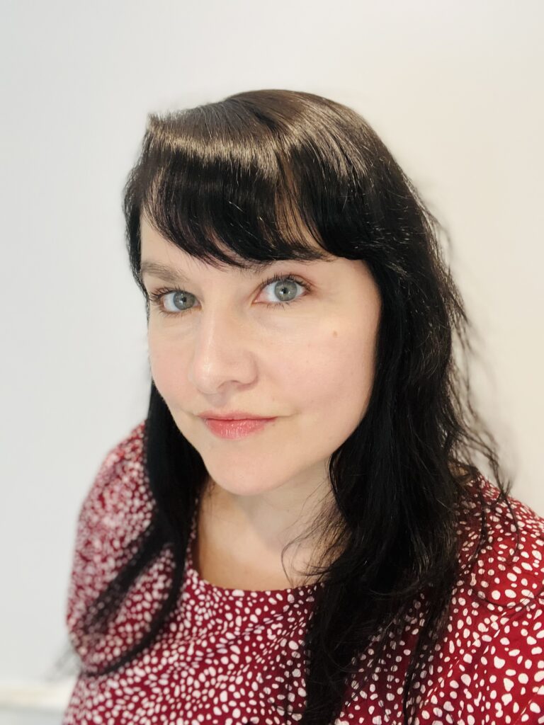 Portrait of a Latinx woman with olive skin, green eyes, black hair, and bangs looking intently at the camera